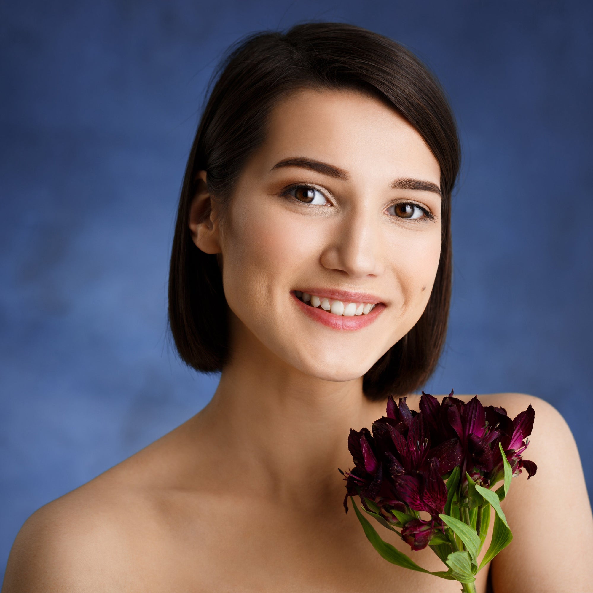 Woman holding a bouquet of dark purple flowers against a blue background
